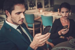 Coppie alla moda con i telefoni cellulari in un ristorante fotografia stock libera da diritti Coppie alla moda con i telefoni cellulari in un ristorante fotografia stock libera da diritti