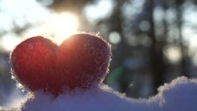Corazón rojo de lana en la nieve y hecho excursionismo por la cámara lenta del sol poniente del invierno Corazón rojo de lana en la nieve y hecho excursionismo por la cámara lenta del sol poniente del invierno