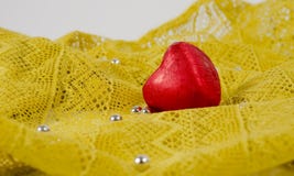 Coração do chocolate em um envoltório vermelho em um fundo do laço amarelo e dos grânulos de prata foto de stock Coração do chocolate em um envoltório vermelho em um fundo do laço amarelo e dos grânulos de prata foto de stock