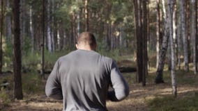 Corredor muscular que corre na estrada com a opinião da parte traseira da floresta Homem atlético que corre na estrada através do filme Corredor muscular que corre na estrada com a opinião da parte traseira da floresta Homem atlético que corre na estrada através do filme