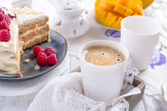 Corte la torta con la crema blanca, para la fruta del mango del desayuno A El fondo blanco, mantel con el cordón, una taza de caf fotografía de archivo Corte la torta con la crema blanca, para la fruta del mango del desayuno A El fondo blanco, mantel con el cordón, una taza de caf fotografía de archivo