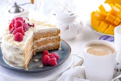 Corte la torta con la crema blanca, para la fruta del mango del desayuno A El fondo blanco, mantel con el cordón, una taza de caf imágenes de archivo libres de regalías Corte la torta con la crema blanca, para la fruta del mango del desayuno A El fondo blanco, mantel con el cordón, una taza de caf imágenes de archivo libres de regalías