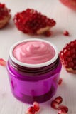Cosmetic cream in a lilac jar and with fresh pomegranate on a white wooden table. pomegranate extract. stock photos Cosmetic cream in a lilac jar and with fresh pomegranate on a white wooden table. pomegranate extract. stock photos