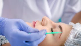 Cosmetologist no revestimento branco do laboratório que aplica a primeira demão ou a testa do desengraxador usando a micro escova video estoque Cosmetologist no revestimento branco do laboratório que aplica a primeira demão ou a testa do desengraxador usando a micro escova video estoque