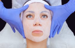 Cosmetologist для процедуры очищать и moisturizing кожу, прикладывая маску листа к стороне молодой женщины стоковое изображение rf Cosmetologist для процедуры очищать и moisturizing кожу, прикладывая маску листа к стороне молодой женщины стоковое изображение rf