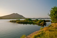 A costa do lago e uma ilha pequena no por do sol iluminam-se Foto de Stock A costa do lago e uma ilha pequena no por do sol iluminam-se Foto de Stock