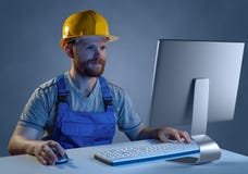 Costruttore del lavoratore in casco e uniforme che funzionano ad un computer, purc fotografie stock Costruttore del lavoratore in casco e uniforme che funzionano ad un computer, purc fotografie stock