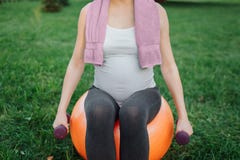Coupez la vue de la jeune femme enceinte s'asseyant sur la boule orange de forme physique en parc Elle tiennent des haltères en m photo libre de droits Coupez la vue de la jeune femme enceinte s'asseyant sur la boule orange de forme physique en parc Elle tiennent des haltères en m photo libre de droits