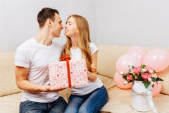 Couple in love, man gives a gift, woman sits at home on the sofa, concept of women`s day royalty free stock photos Couple in love, man gives a gift, woman sits at home on the sofa, concept of women`s day royalty free stock photos