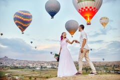 Couple in love stands on background of balloons in Cappadocia. Man and a woman on hill look at a large number of flying balloons Stock Photos Couple in love stands on background of balloons in Cappadocia. Man and a woman on hill look at a large number of flying balloons Stock Photos