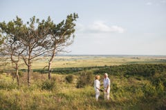 A couple of senior adults in the white linen dress is standing outdoors, in the hands a bouquet of flowers, three royalty free stock photography A couple of senior adults in the white linen dress is standing outdoors, in the hands a bouquet of flowers, three royalty free stock photography