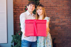 Couple Sharing Christmas Present. Young family embracing and holding red gift box at home with decorations Stock Photo Couple Sharing Christmas Present. Young family embracing and holding red gift box at home with decorations Stock Photo