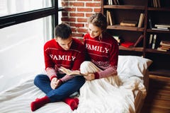 Couples dans le livre rouge de lecture de chandails dans le lit ensemble photos stock Couples dans le livre rouge de lecture de chandails dans le lit ensemble photos stock