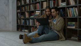 Couples de sourire d'étudiant utilisant le PC de comprimé dans la bibliothèque banque de vidéos Couples de sourire d'étudiant utilisant le PC de comprimé dans la bibliothèque banque de vidéos