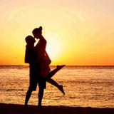 Couples romantiques sur la plage au coucher du soleil coloré sur le fond Photographie stock Couples romantiques sur la plage au coucher du soleil coloré sur le fond Photographie stock