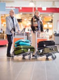 Couples supérieurs d'affaires marchant avec le bagage dans des chariots chez Airpo photos libres de droits Couples supérieurs d'affaires marchant avec le bagage dans des chariots chez Airpo photos libres de droits