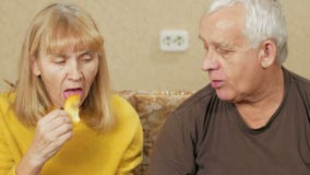 Couples supérieurs mangeant du fruit à la maison sur le divan La femme a découpé un morceau de kaki et donne à des hommes le poid clips vidéos Couples supérieurs mangeant du fruit à la maison sur le divan La femme a découpé un morceau de kaki et donne à des hommes le poid clips vidéos