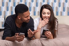 Couplez dans l'amour détendant ensemble tout en se trouvant sur le lit Jeune homme et femme regardant le téléphone portable avec image libre de droits Couplez dans l'amour détendant ensemble tout en se trouvant sur le lit Jeune homme et femme regardant le téléphone portable avec image libre de droits