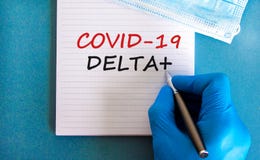 Covid-19 delta plus variant strain symbol. Hand in blue glove with white card. Concept words Covid-19 delta plus variant. Metalic