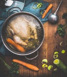 Cozimento da canja de galinha, potenciômetro com caldo de galinha e concha no fundo de madeira rústico escuro com ingredientes do Imagem de Stock Royalty Free Cozimento da canja de galinha, potenciômetro com caldo de galinha e concha no fundo de madeira rústico escuro com ingredientes do Imagem de Stock Royalty Free