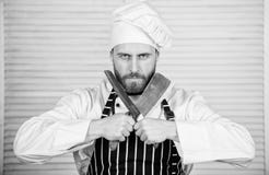 Cozinha perigosa cozinheiro chefe pronto para cozinhar homem seguro na faca da posse do avental e do chap?u alimento farpado dos imagem de stock Cozinha perigosa cozinheiro chefe pronto para cozinhar homem seguro na faca da posse do avental e do chap?u alimento farpado dos imagem de stock