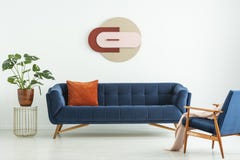 Creative geometric art on a white wall above an elegant blue sofa in a mid-century modern style living room interior. Real photo.