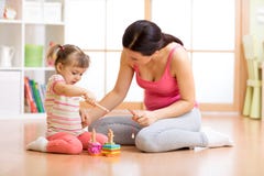 Criança bonita que joga com os brinquedos com mãe feliz dentro fotografia de stock Criança bonita que joga com os brinquedos com mãe feliz dentro fotografia de stock