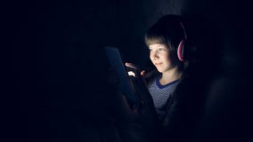 A criança em fones de ouvido sem fio escuta a música na noite sob uma cobertura e olha a tabuleta video estoque A criança em fones de ouvido sem fio escuta a música na noite sob uma cobertura e olha a tabuleta video estoque