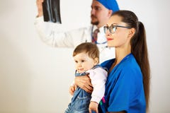 A criança está sentando-se nas mãos do doutor, o segundo doutor olha o raio X Fundo branco imagens de stock A criança está sentando-se nas mãos do doutor, o segundo doutor olha o raio X Fundo branco imagens de stock