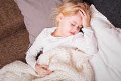 A criança pequena que é doente e que guarda sua mão pressionou contra sua testa imagem de stock A criança pequena que é doente e que guarda sua mão pressionou contra sua testa imagem de stock