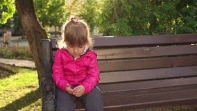 Criança triste que senta-se em um banco no parque filme Criança triste que senta-se em um banco no parque filme