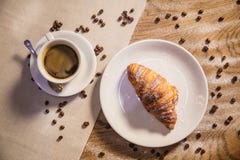 Croissant and coffee on a wooden table, coffee grains scattered on a table stock photo Croissant and coffee on a wooden table, coffee grains scattered on a table stock photo