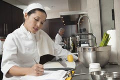 Cuoco unico femminile Writing On Clipboard in cucina immagini stock libere da diritti Cuoco unico femminile Writing On Clipboard in cucina immagini stock libere da diritti