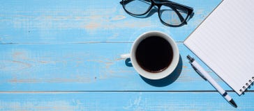 Cup of black coffee with office supplies; pen, notebook and eyes glasses on blue wooden table background royalty free stock photos Cup of black coffee with office supplies; pen, notebook and eyes glasses on blue wooden table background royalty free stock photos