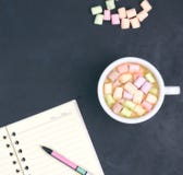 Cup with coffee and marshmallows, blank open notebook with pen on abstract black background. View from above. Flat layout. space stock photography Cup with coffee and marshmallows, blank open notebook with pen on abstract black background. View from above. Flat layout. space stock photography