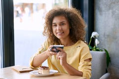 Curly girl with beatiful smile keeping cup of coffee, looking at camera. stock photo Curly girl with beatiful smile keeping cup of coffee, looking at camera. stock photo