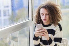 Curly Hair Teen Girl With Mobile Phone By Window Stock Images