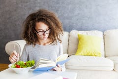 Curly Hair Teenage Girl Reading Book And Eating Salad Stock Image