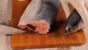 Cut fish on a wooden Board. Pink salmon is already on the table. Cutting off the head and tail of a sea fish with a