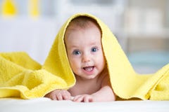 Cute baby covered with a bath towel lying on tummy in the bathroom