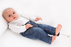 Cute baby lying barefoot on white sofa wearing blue denim jeans. Alone and sad Stock Photo Cute baby lying barefoot on white sofa wearing blue denim jeans. Alone and sad Stock Photo