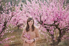 Cute beautiful stylish dressed brunette girl with mother mom standing on a field of spring young peach tree with pink stock image Cute beautiful stylish dressed brunette girl with mother mom standing on a field of spring young peach tree with pink stock image