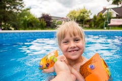 A cute blond baby girl swims at swimmig pool with blue colored water outdoors, smiles and hold parent`s hand. stock photography A cute blond baby girl swims at swimmig pool with blue colored water outdoors, smiles and hold parent`s hand. stock photography