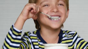 Cute boy European appearance is yogurt. Portrait of a happy child sitting at the table. Ecco, baby food. stock footage Cute boy European appearance is yogurt. Portrait of a happy child sitting at the table. Ecco, baby food. stock footage