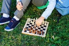 Cute boy in riound glasses and blue shirt sits on the grass in the park and plays chess at wooden chessboard. Hobby, education stock photography Cute boy in riound glasses and blue shirt sits on the grass in the park and plays chess at wooden chessboard. Hobby, education stock photography