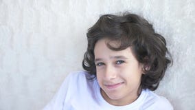 Cute curly-haired boy the teenager looks into the camera laughing and makes a funny facial expression. 4k, slow motion stock video footage Cute curly-haired boy the teenager looks into the camera laughing and makes a funny facial expression. 4k, slow motion stock video footage