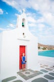 Cute Girl In Blue Dress Outdoors Near Church. Kid At Street Of Typical Greek Traditional Village On Mykonos Island Stock Image
