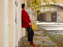 Cute girl in a knitted hat red jacket and red boots standing near a wall in full growth in the outdoor royalty free stock images Cute girl in a knitted hat red jacket and red boots standing near a wall in full growth in the outdoor royalty free stock images
