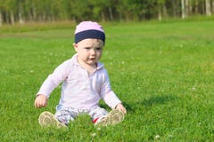 Cute happy baby girl in hat sits on green grass stock photo Cute happy baby girl in hat sits on green grass stock photo