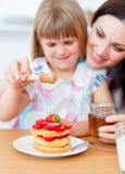 Cute lgirl and her mother putting honey on waffles stock image Cute lgirl and her mother putting honey on waffles stock image
